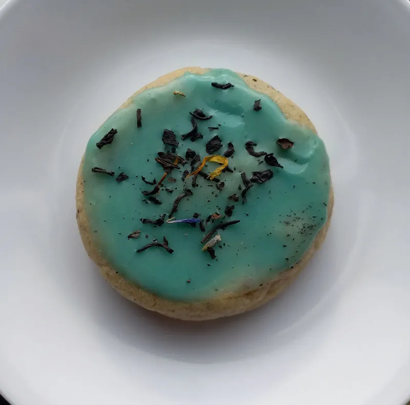 a round cookie with blue icing, topped with loose tea leaves and flower petals