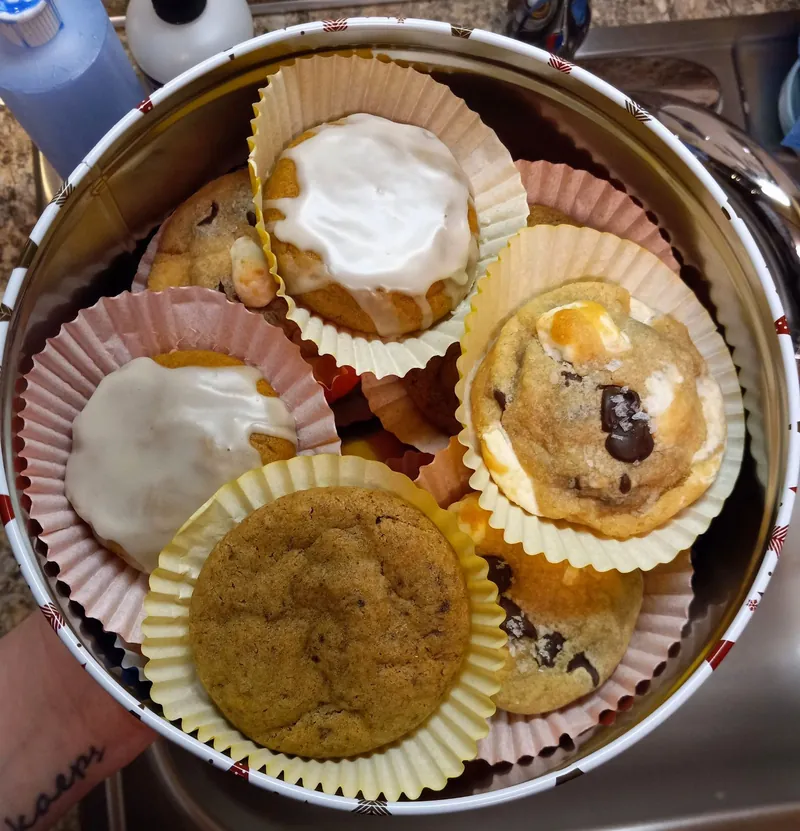 a cookie tin filled with iced cookies and chocolate chip cookies in paper liners