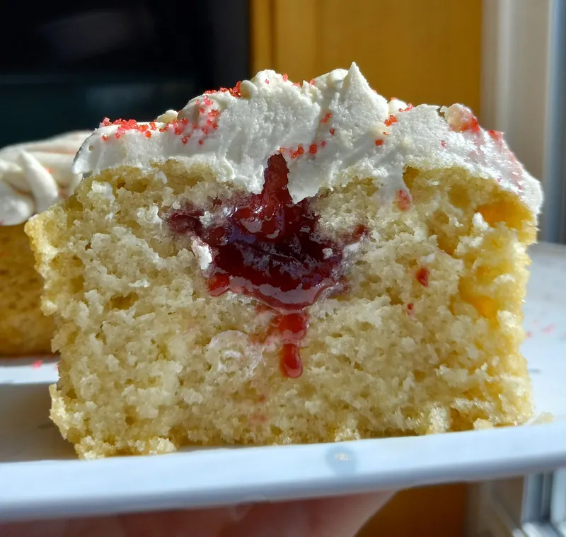 a vanilla cupcake cut open to show a jam center, with red sugar on the frosting