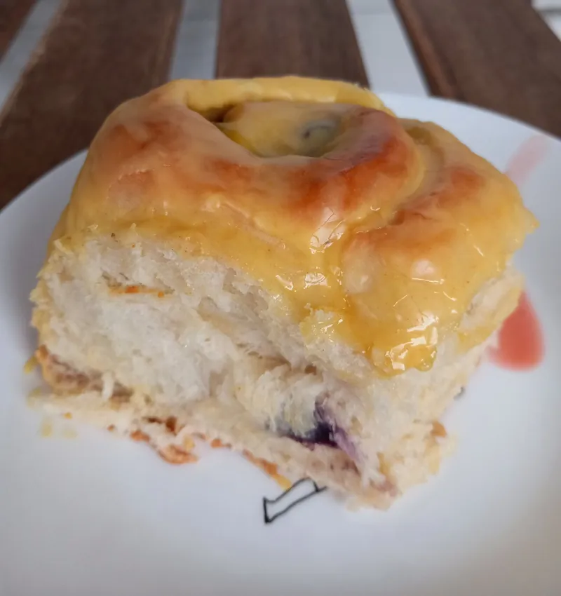 a lemon blueberry milk bread cinnamon roll under a yellow glaze, cut open to show the blueberry filling
