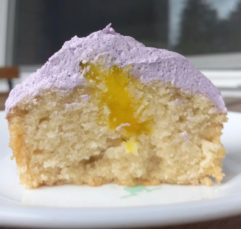 a lemon curd cupcake with ube buttercream, cut open to show the lemon curd center