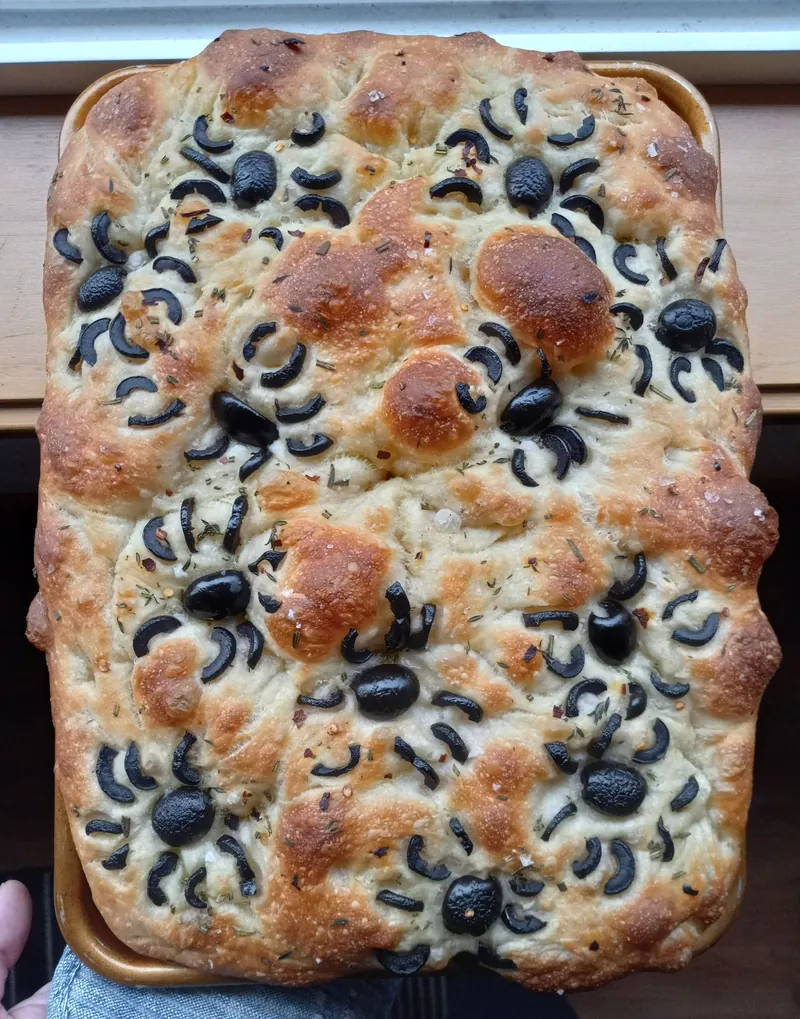 a pan of focaccia decorated with black olive spiders