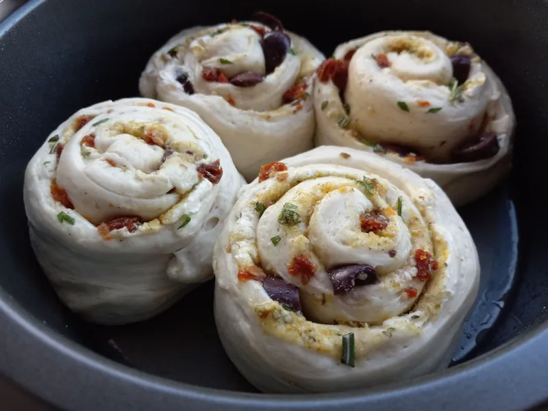 savory swirl rolls with olives, sun-dried tomatoes and herbs in a pan, before baking
