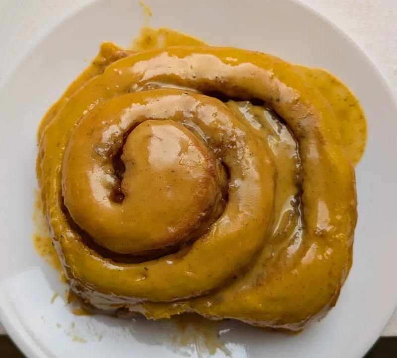a pumpkin milk bread cinnamon roll with golden milk latte frosting