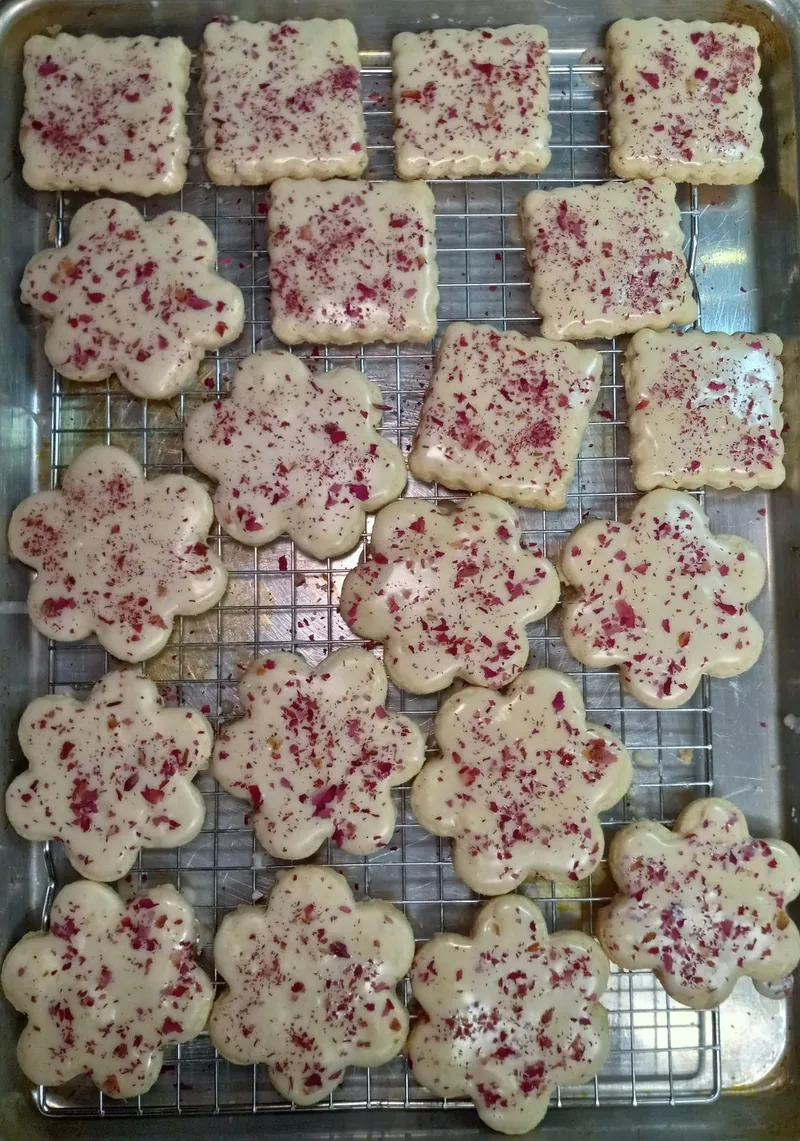 a rack of flower and square sugar cookies with white icing and dried rose petals