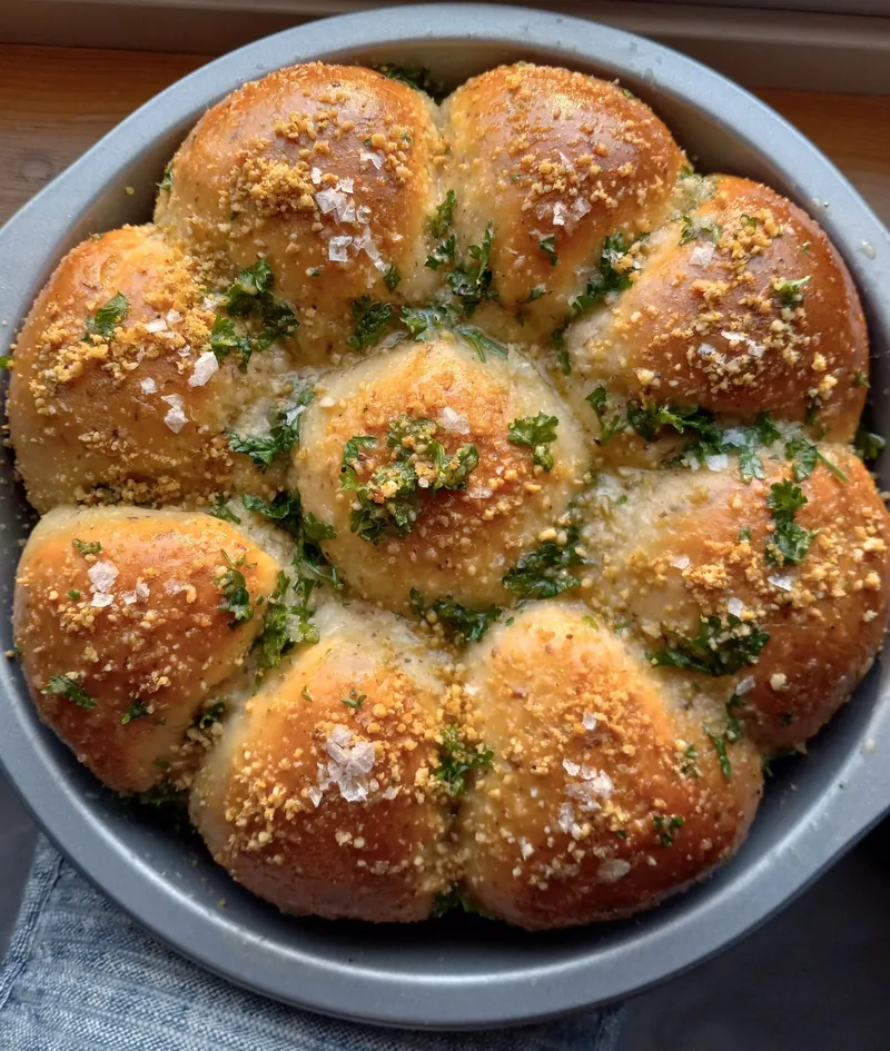 a round pan of sourdough garlic herb buns, topped with fresh herbs and flaky salt