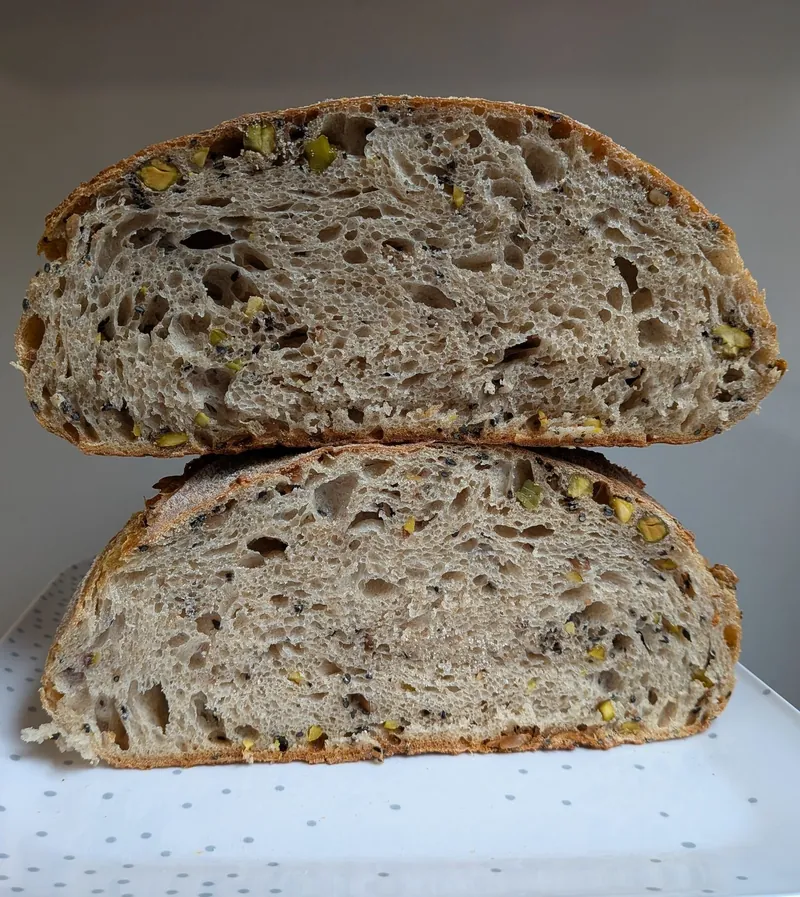 a loaf of seeded spelt sourdough with pistachios, cut to show the crumb